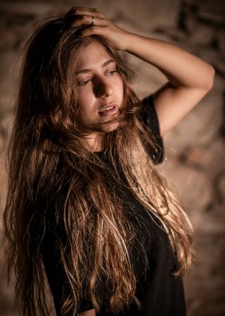 Junge Frau mit langen offenen Haaren lehnt an einer Steinwand