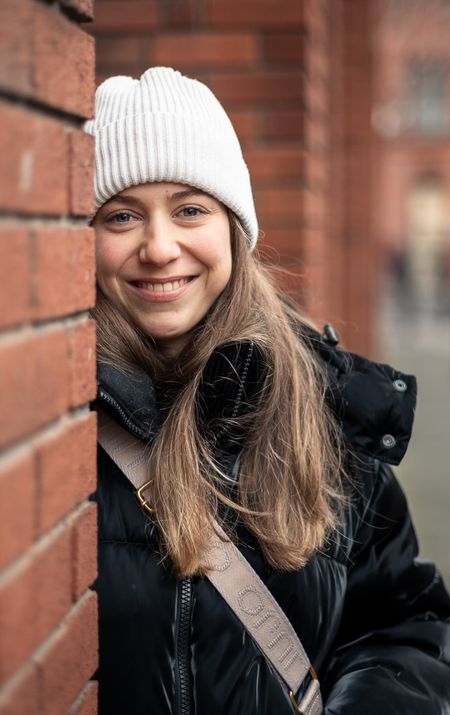 Junge Frau mit weisser Mütze lächelt vor einer Backsteinwand