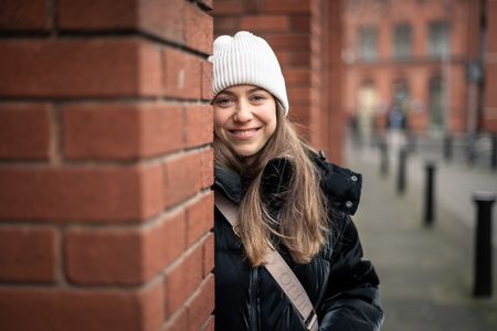 Junge Frau mit weisser Mütze lächelt vor einer Backsteinwand