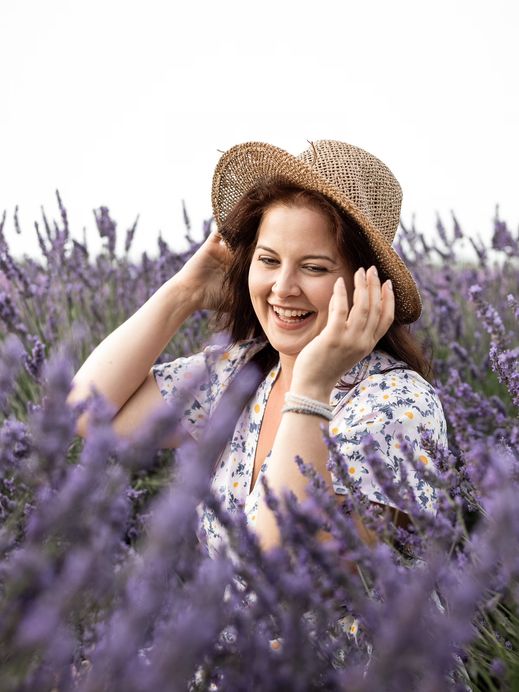 Frau hält lachend ihren Strohhut fest, im Vordergrund blühender Lavendel