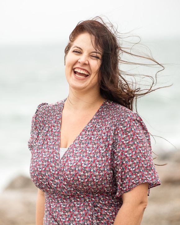 Frau im geblümten Kleid lacht, der Wind fährt ihr durchs Haar