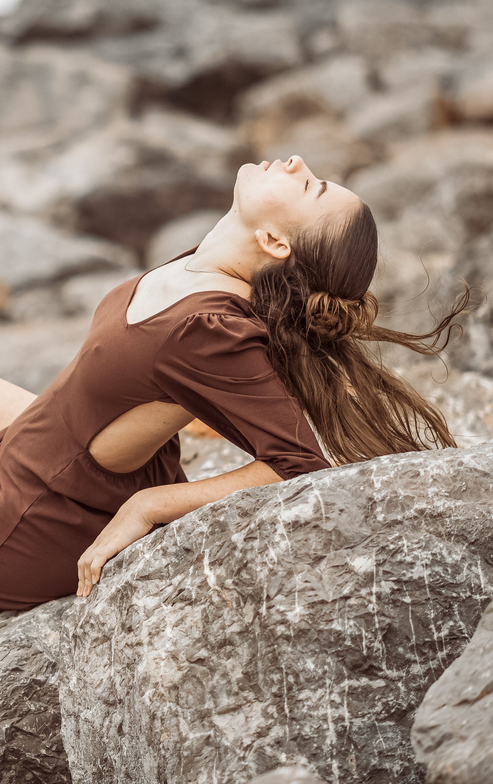 Frau im braunen Kleid liegt auf Felsen am Meer und blickt nach oben
