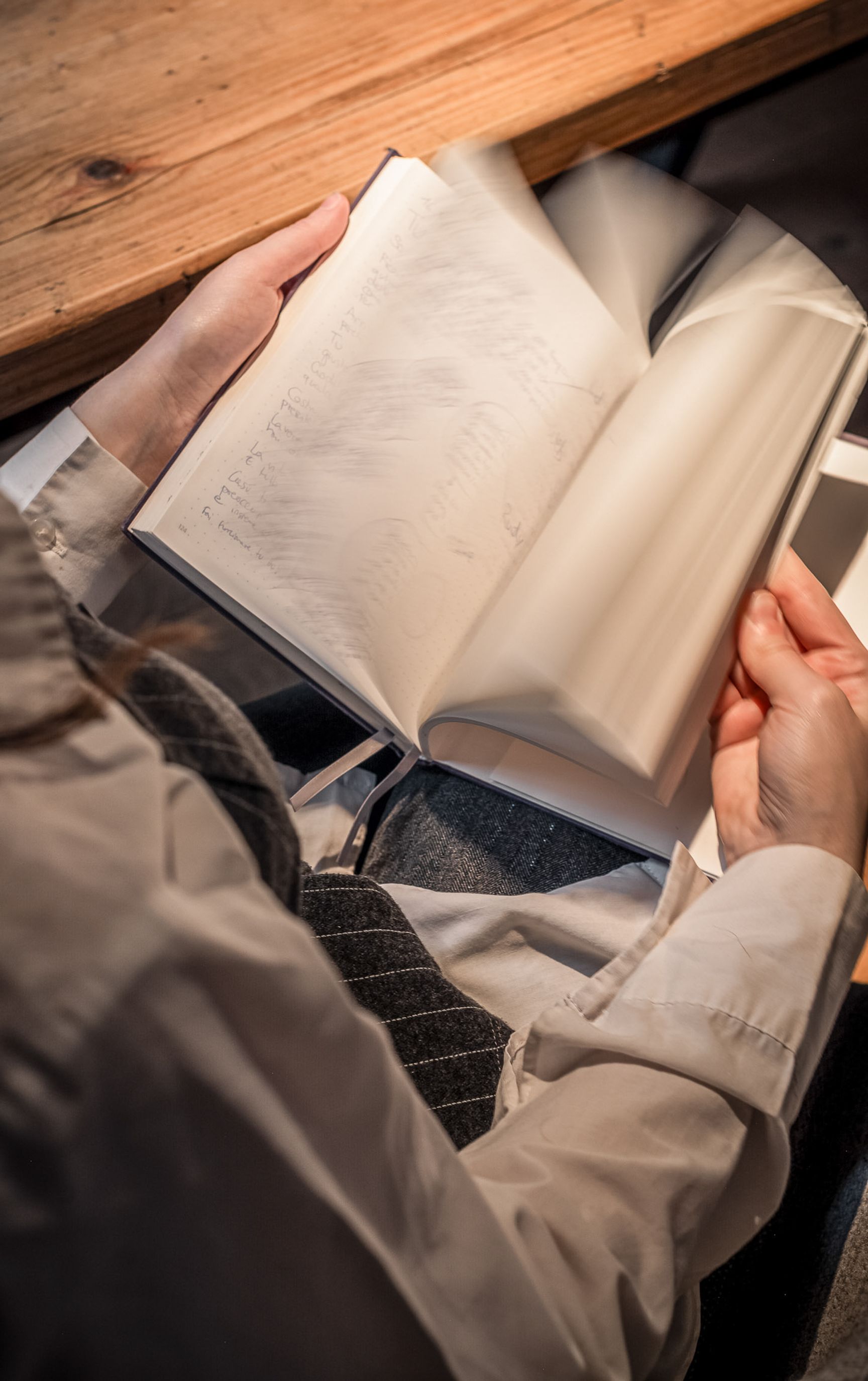 Hände blättern in einem aufgeschlagenen Buch auf einem Holztisch