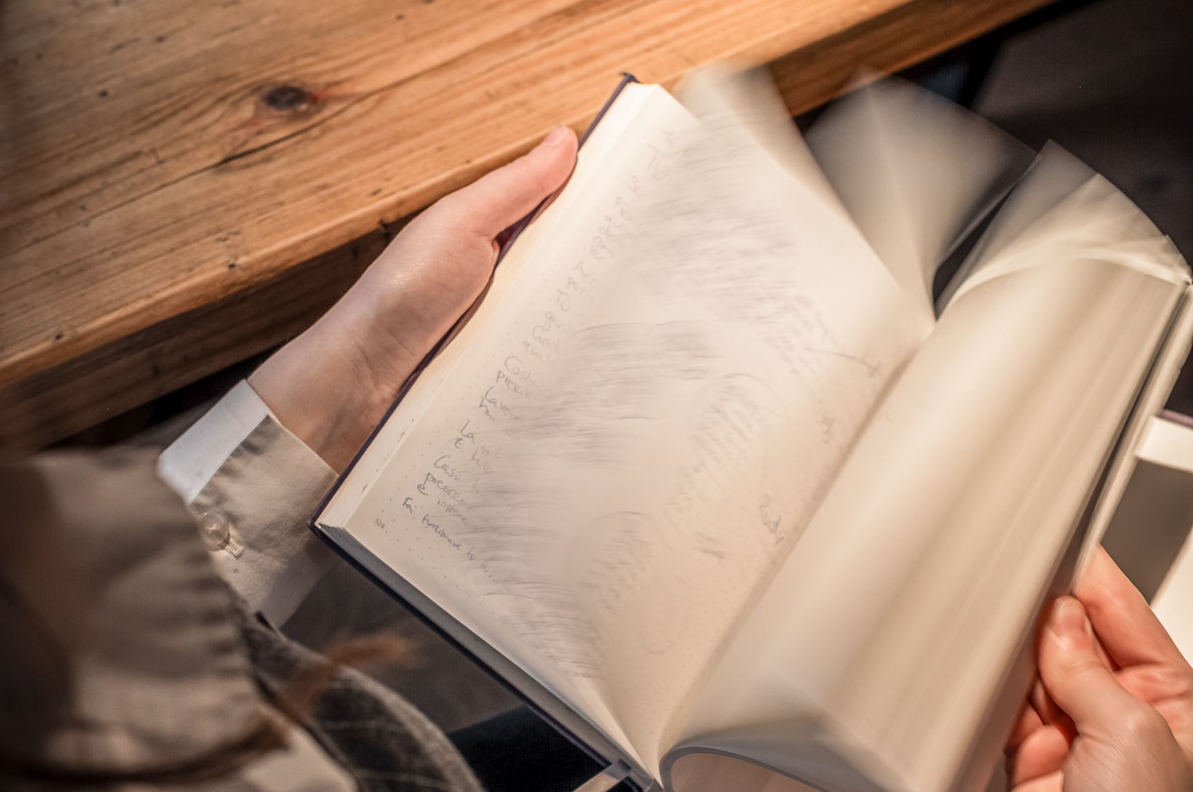 Hände blättern in einem aufgeschlagenen Buch auf einem Holztisch