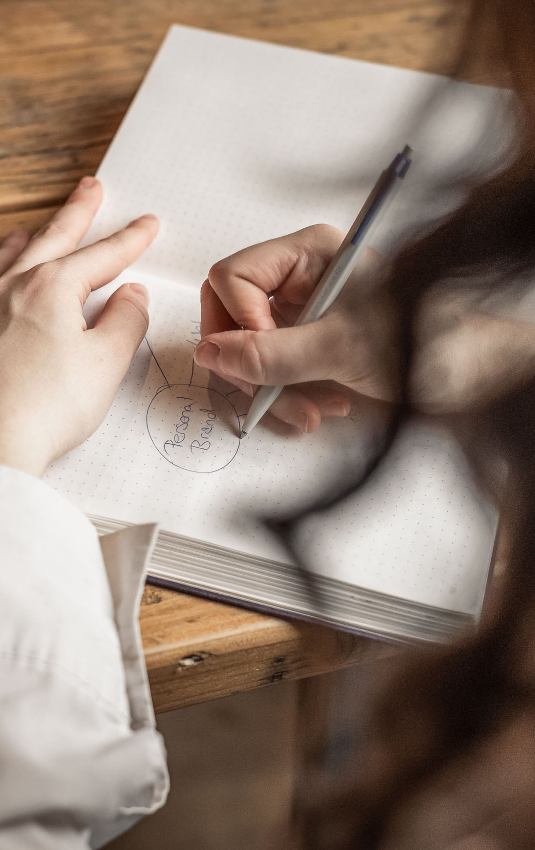 Eine Frau schreibt an einem Holztisch in ein Notizbuch und zeichnet ein Diagramm um das Wort «Personal Brand»