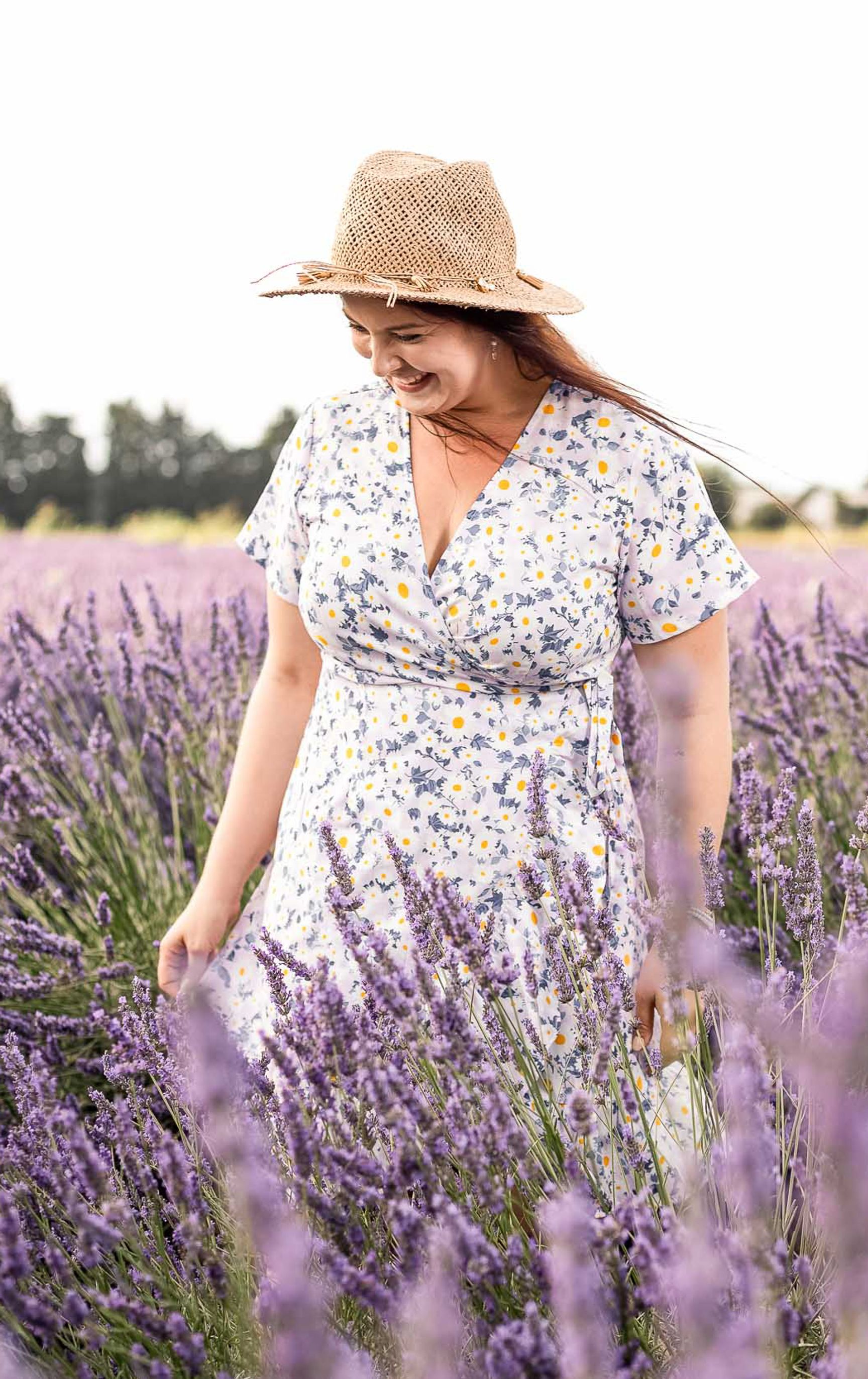 Frau im geblümten Sommerkleid mit Strohhut geht durch ein blühendes Lavendelfeld