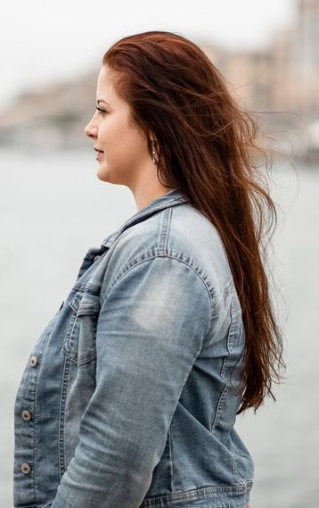 Frau in Jeansjacke steht im Profil am Ufer, der Wind bewegt ihr Haar