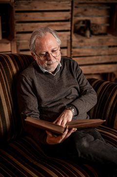 Älterer Mann blättert in einem Fotoalbum auf einem gestreiften Sofa