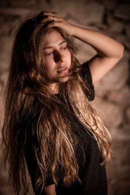 Junge Frau mit langen offenen Haaren vor einer rauen Steinwand