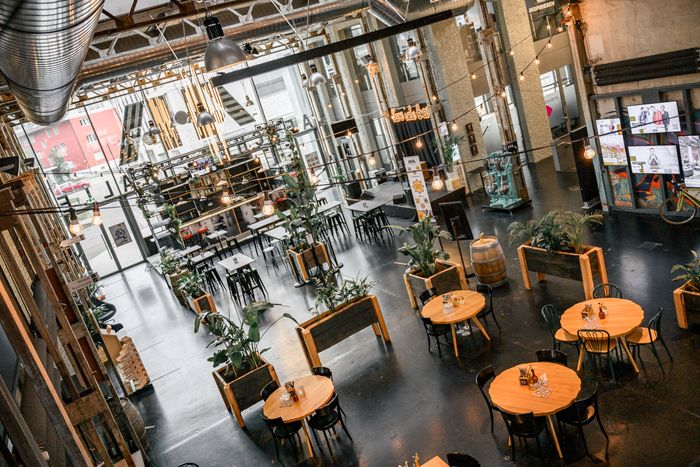 Blick von oben in die Aeschbachhalle: Industriehalle mit Lichterketten, runden Holztischen, Pflanzen und Bar