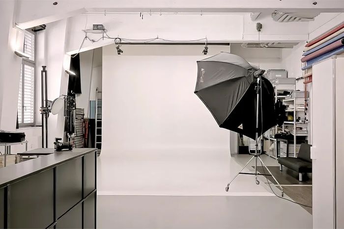Helles Fotostudio mit weisser Hohlkehle, Studioblitz mit grossem Softbox-Schirm und Arbeitstheke