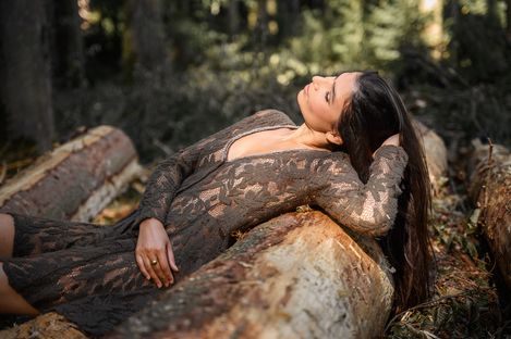Frau lehnt an einem alten Baumstamm im Wald und blickt nach oben