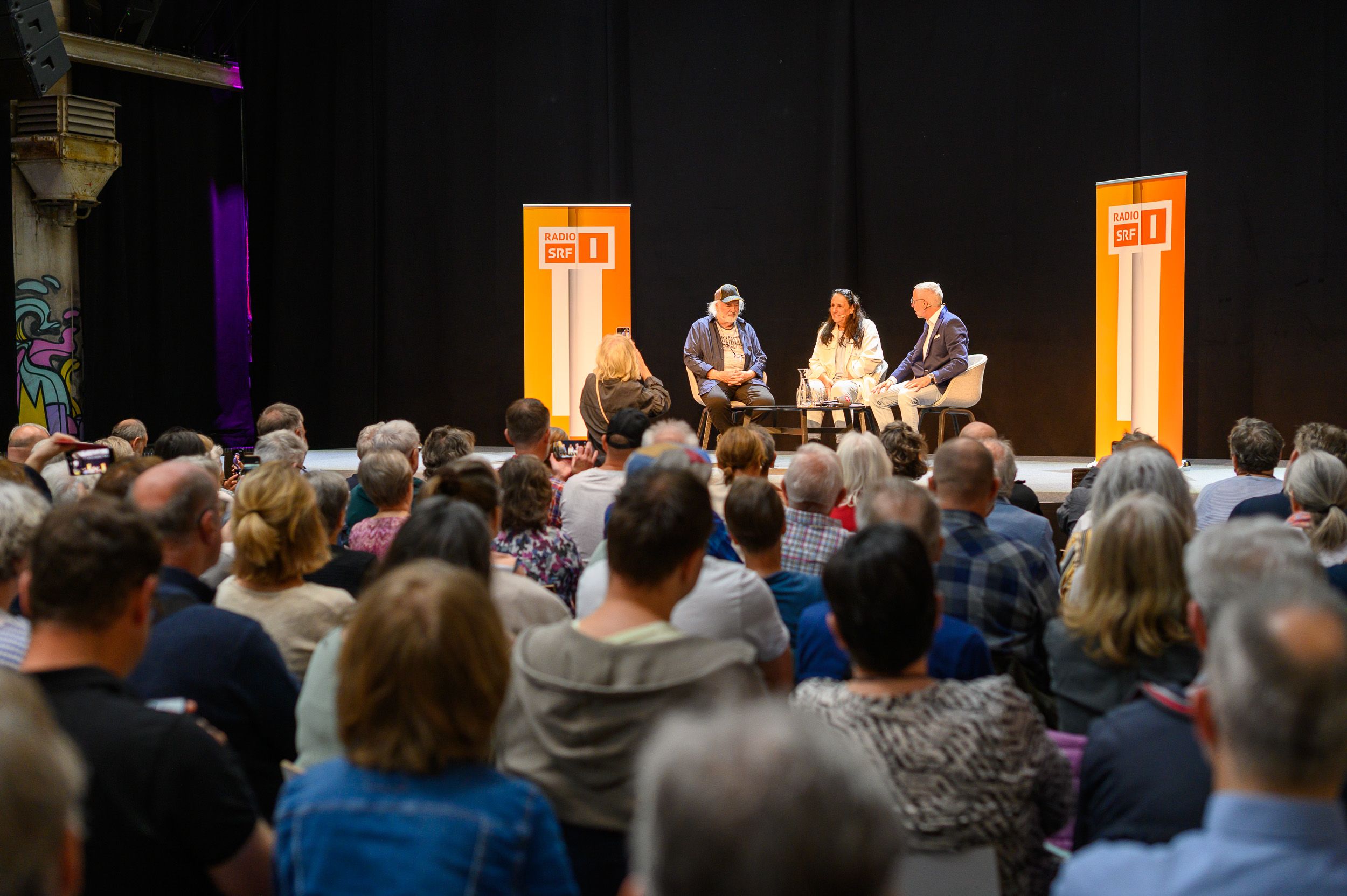 Podiumsgespräch auf der Bühne, davor das Publikum von hinten