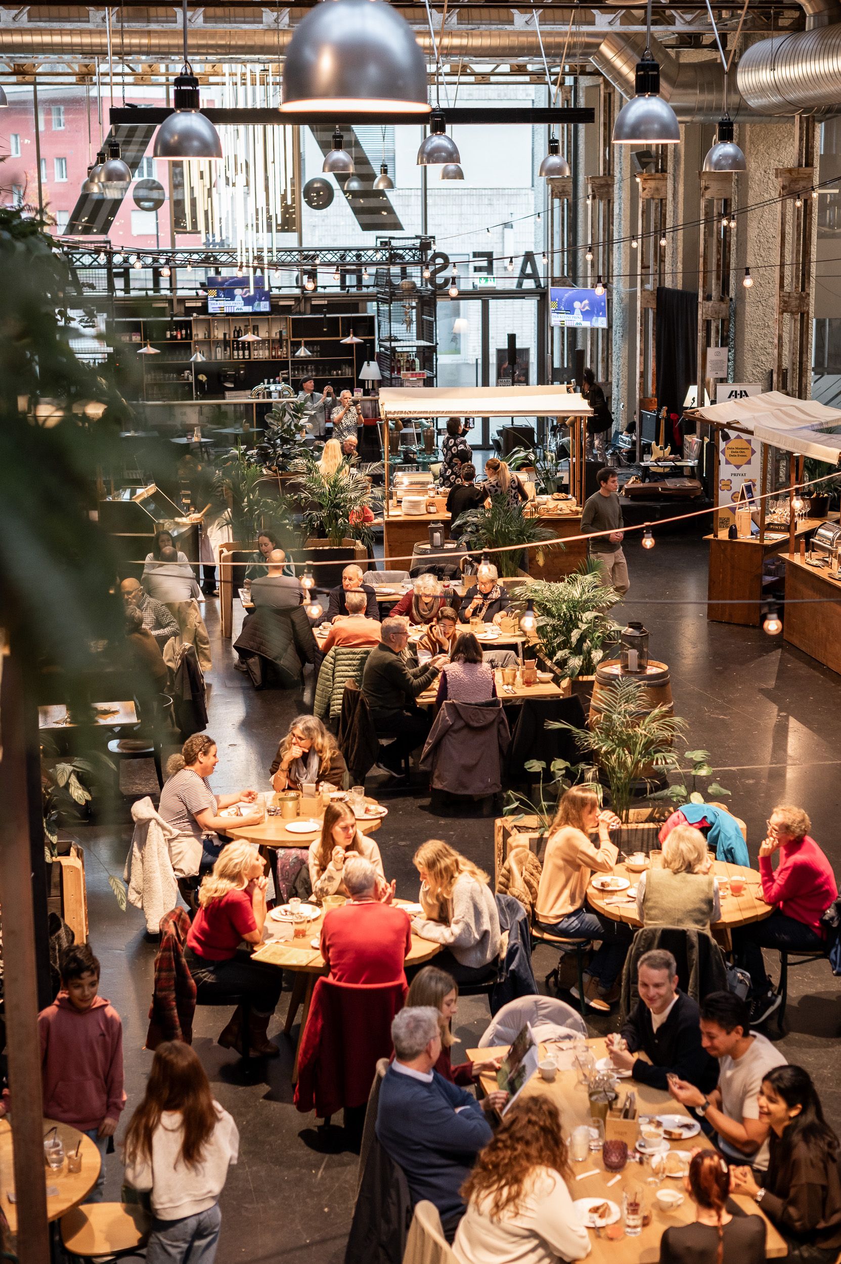 Blick von oben in die Halle: lange Tischreihen, Pflanzen und Lichterketten