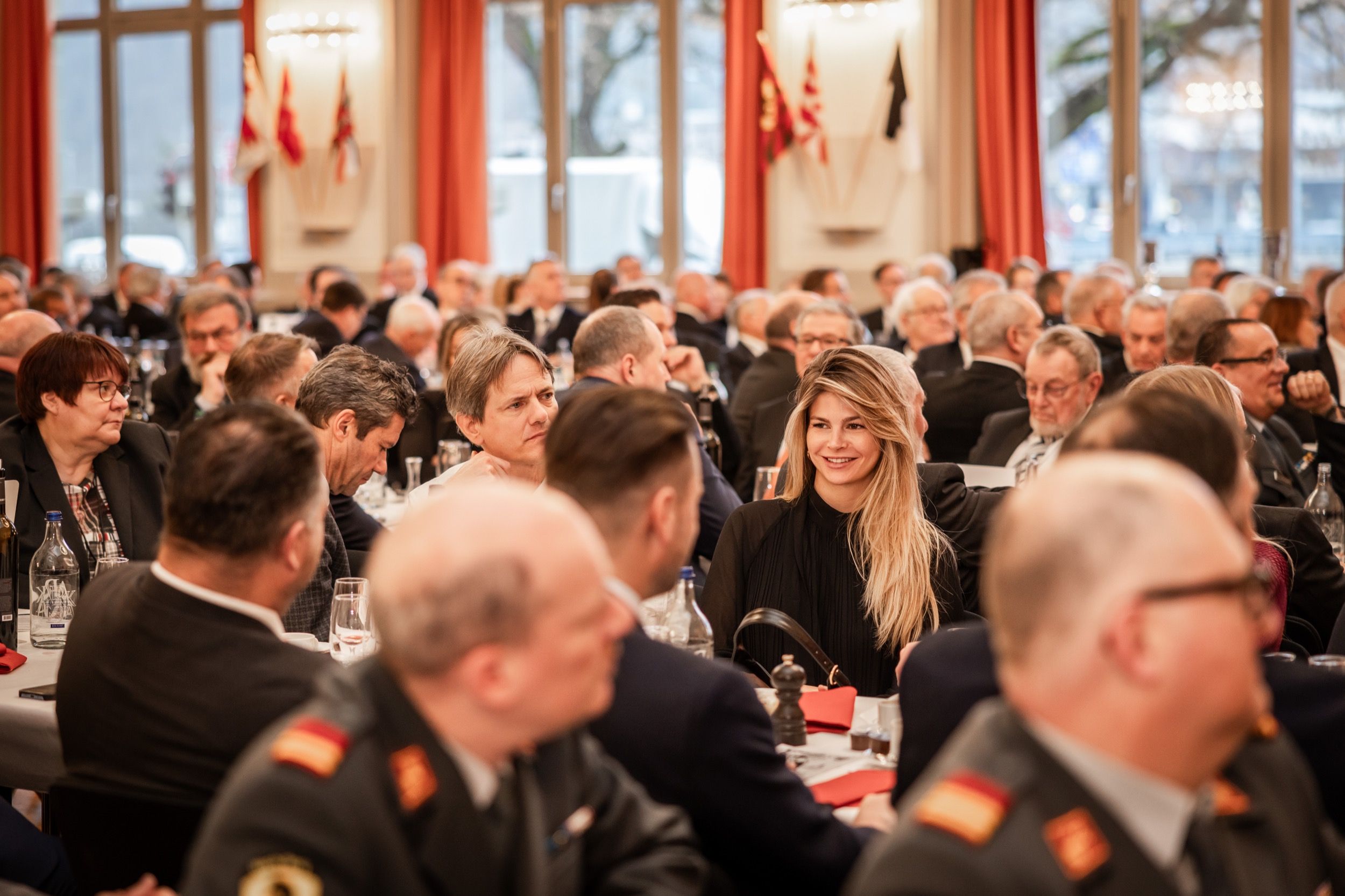 Gäste in Uniform und festlicher Kleidung an langen Tischen im Saal