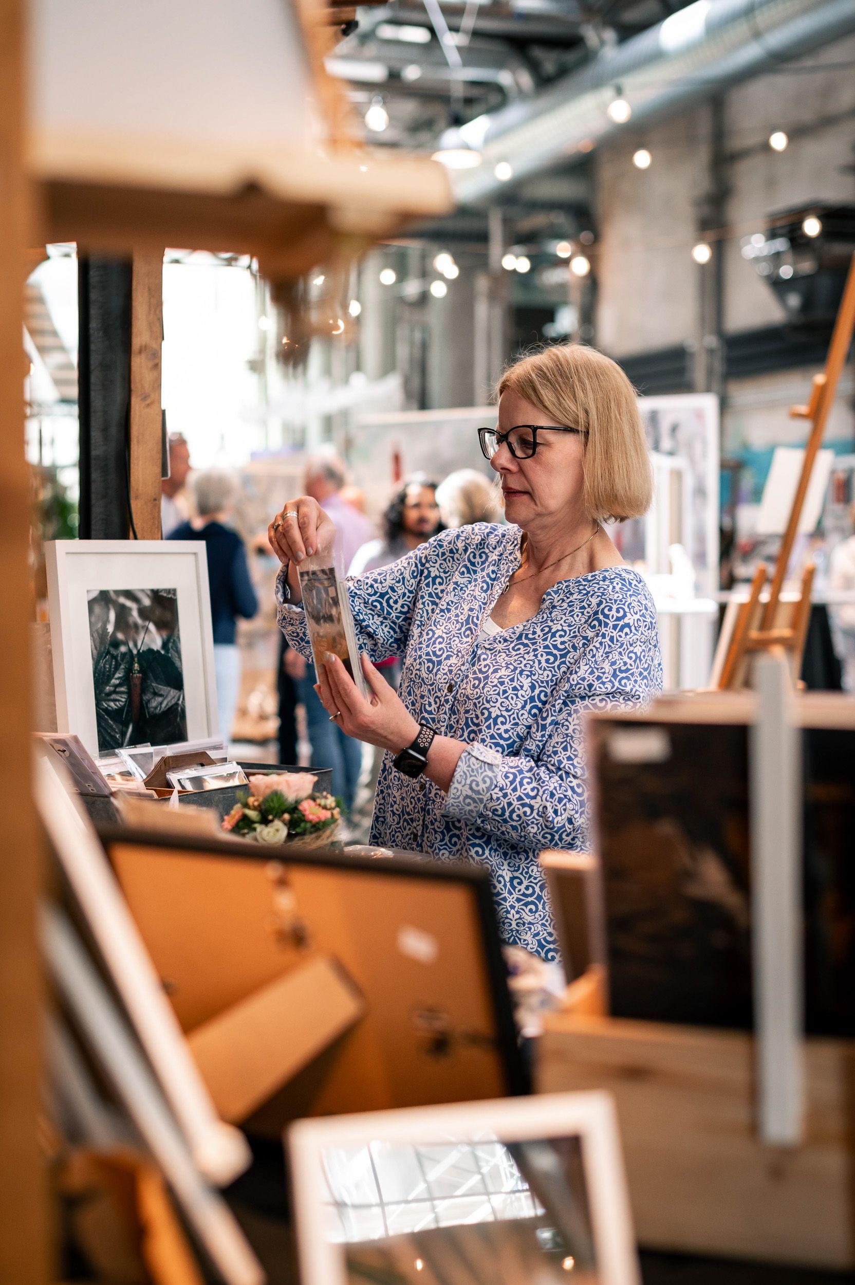 Frau im Gespräch an ihrem Messestand, umgeben von Bildern und Dekoration
