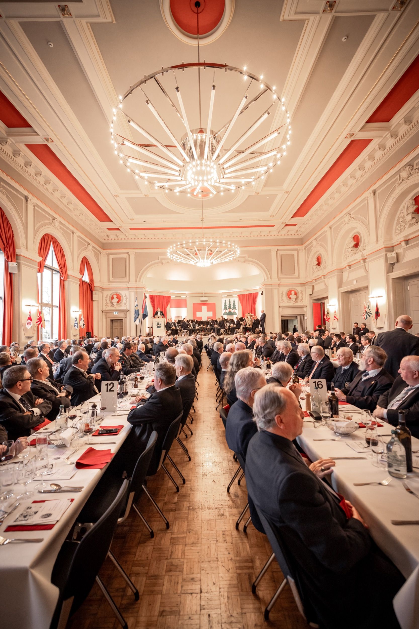 Festsaal von oben: lange gedeckte Tische voller Gäste, Kronleuchter und rote Wände