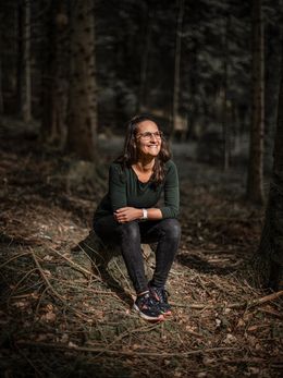 Frau mit Brille sitzt auf einem Baumstumpf im Wald