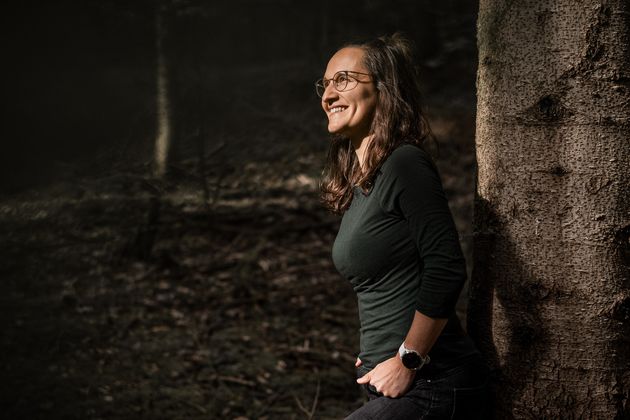 Sara lehnt an einem Baum im Wald und lacht ins Sonnenlicht