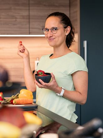 Sara hält eine Schale mit Erdbeeren und nimmt eine davon heraus