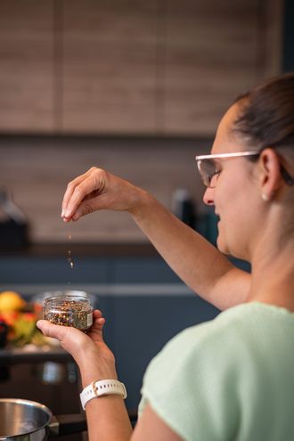 Sara streut Gewürze aus einem Glas, von hinten über die Schulter fotografiert