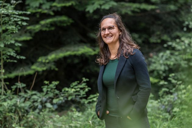 Sara im dunklen Blazer steht im Grünen und lacht