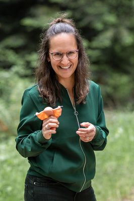 Sara hält ein kleines orangefarbenes Modell in der Hand und lacht in die Kamera