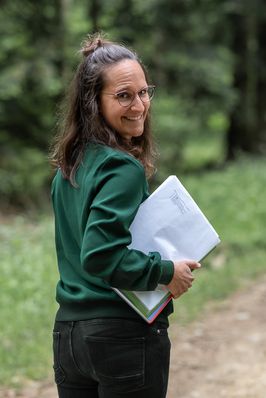 Sara schaut über die Schulter zurück, unter dem Arm Unterlagen