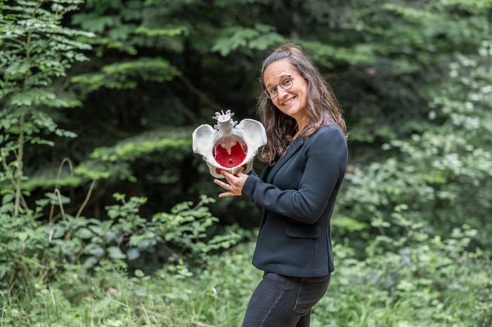 Sara steht im Grünen und hält ein anatomisches Beckenmodell in den Händen