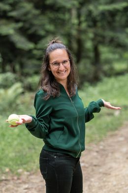 Sara hält einen Tennisball in der Hand, die Arme leicht ausgebreitet, auf einem Waldweg