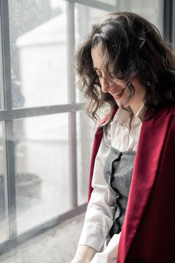 Simona im roten Mantel am Fenster, den Blick gesenkt
