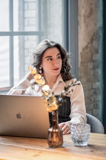 Simona am Laptop an einem Holztisch, den Blick zur Seite gewandt