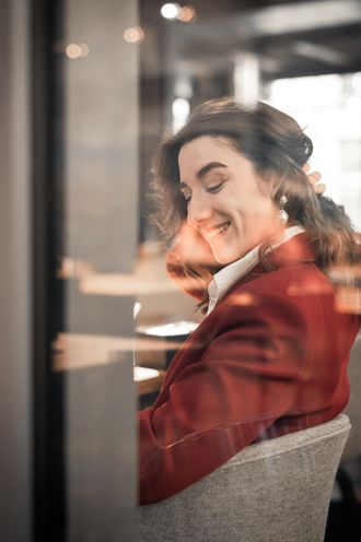 Simona im weinroten Blazer lacht mit geschlossenen Augen, Spiegelung im Fensterglas