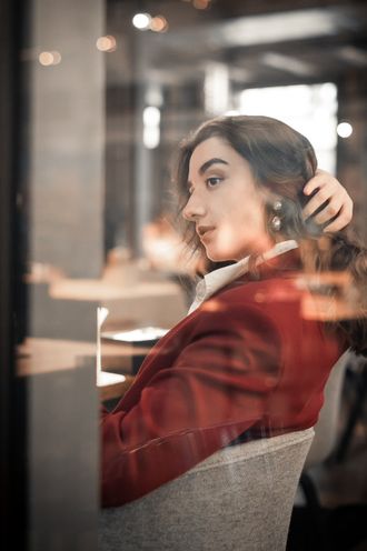 Simona im weinroten Blazer schaut über die Schulter, Spiegelung im Fensterglas