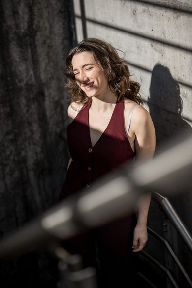 Simona im weinroten Kleid auf einer Treppe im Sonnenlicht