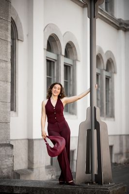 Simona im weinroten Anzug steht auf einer Treppe vor einem Altbau