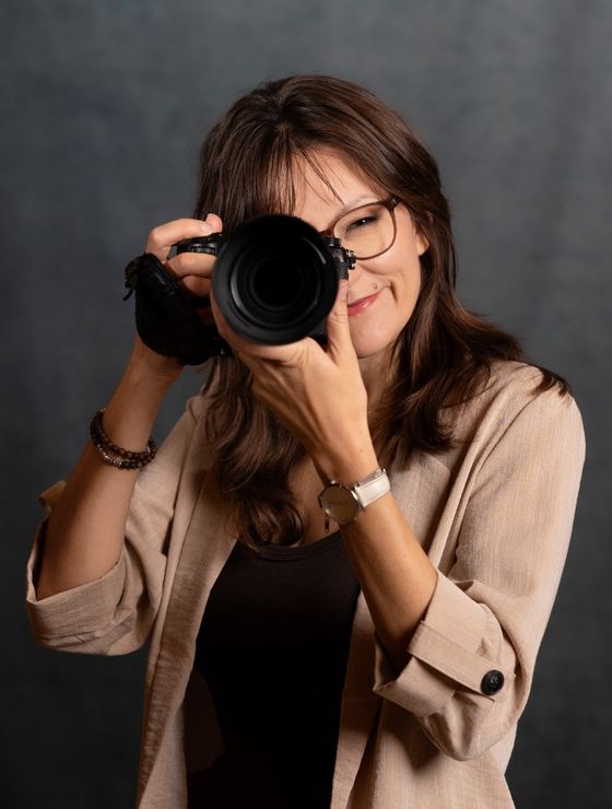 Seraina Wild mit Brille schaut lächelnd durch ihre Kamera, dunkler Hintergrund