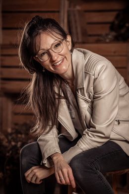 Seraina Wild in heller Lederjacke sitzt vor einer Holzwand und lächelt