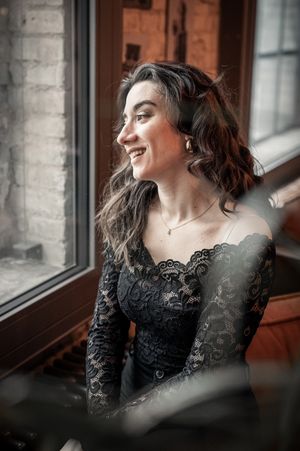 Junge Frau im schwarzen Spitzenkleid sitzt an einem Fenster und lacht zur Seite